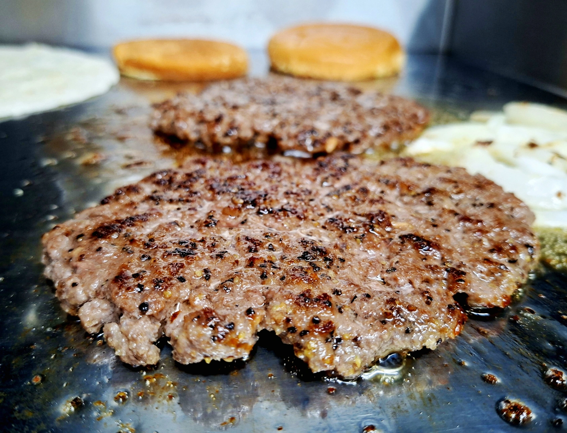 Seasoned beef patties searing on the griddle